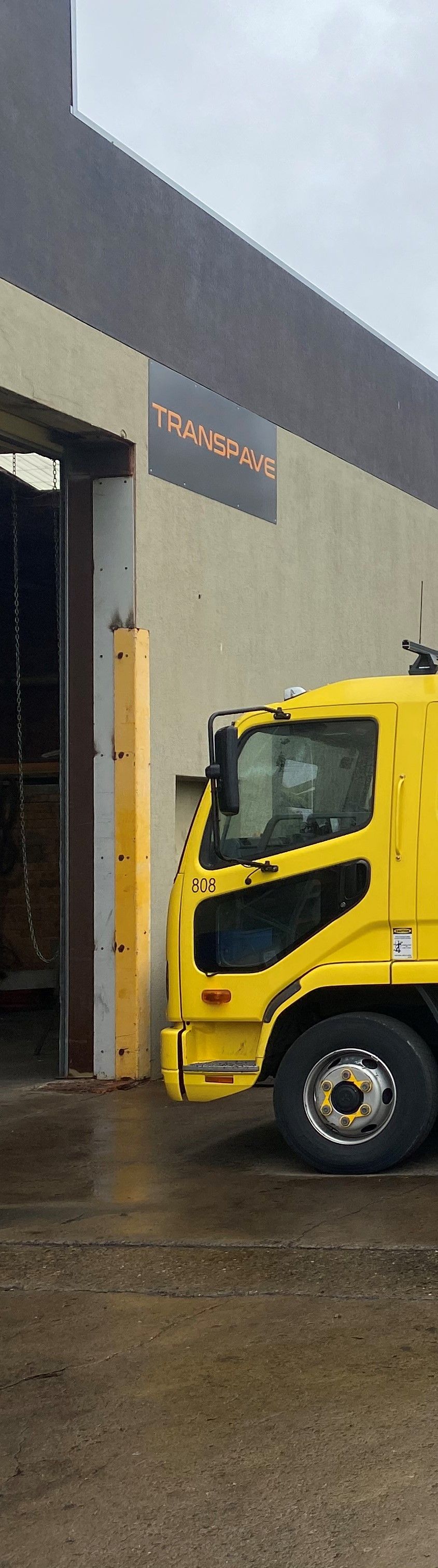 Picture of a yellow cab chassis parked out the front of a factory with the Transpave sign on it.