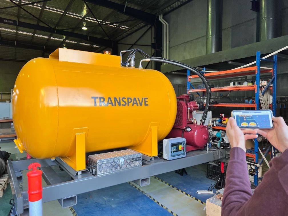 Image of a yellow emulsion tank and compressor mounted on a skid being operated by a mobile phone